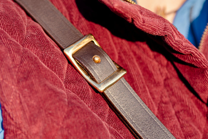 Close up on a sort of red corduroy jacket with a leather dog harness slung over the shoulder.