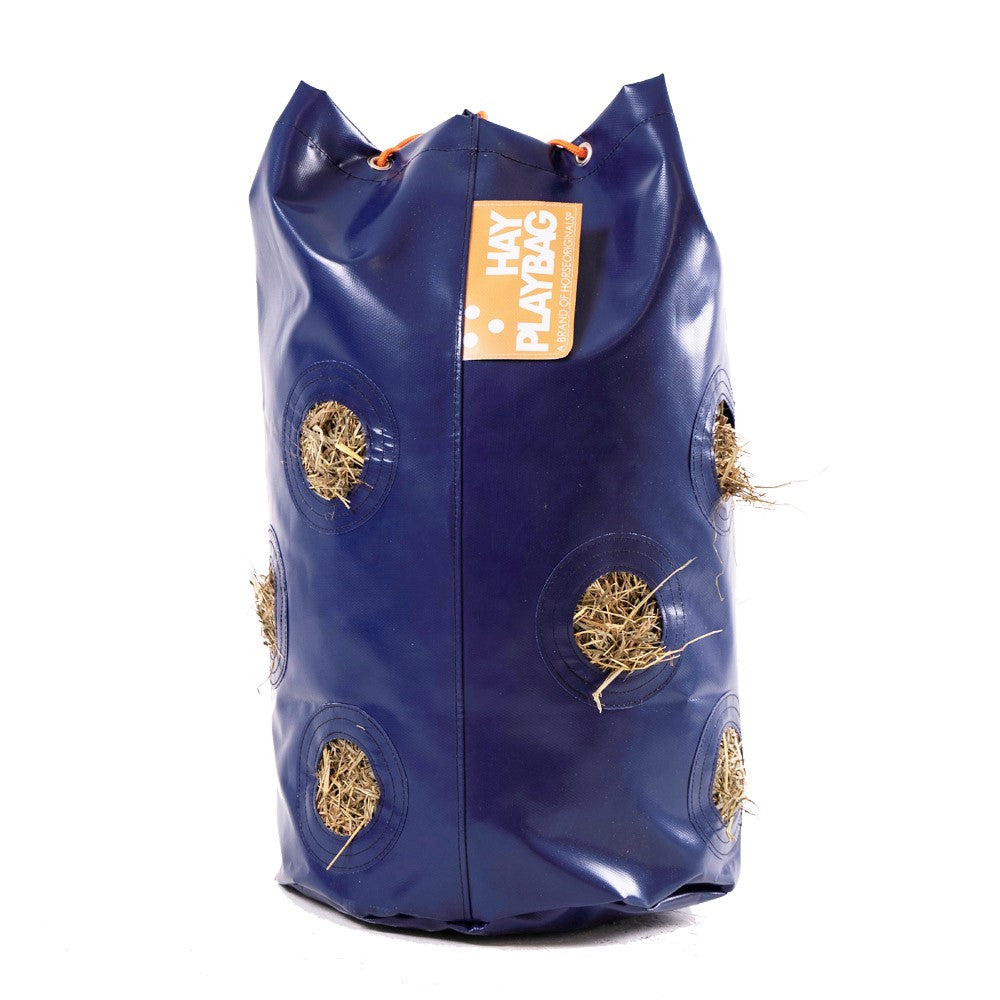 A cylindrical blue bag with 6 visible holes. Hay fills the bag and pokes out of the holes.