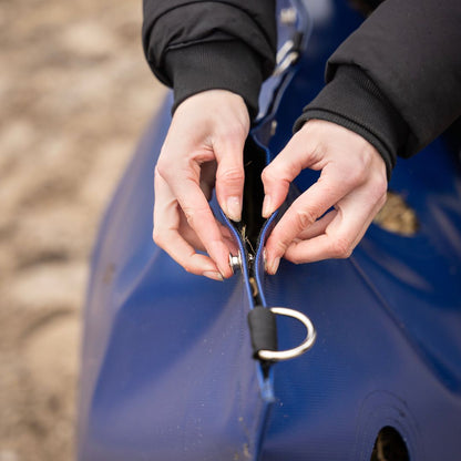 Person opening a blue bag with a metal snap system for feeding horses hay